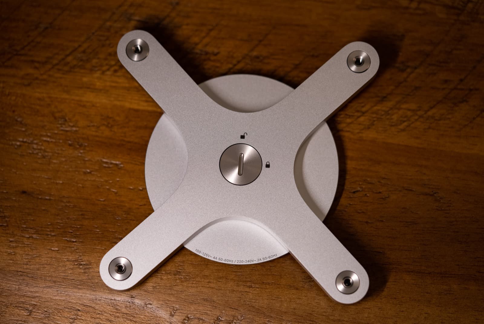 Apple Pro Display XDR VESA mount adapter on a wooden surface, showing the standard 100x100 mm four-hole pattern
